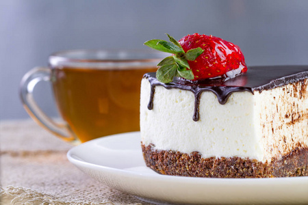 一杯热茶和一片甜蛋糕，上面有新鲜的草莓和白色盘子里滴着巧克力釉。 甜点心