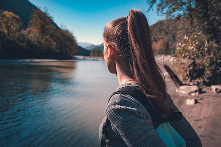 一个带着蓝色背包的年轻女孩旅行者站在山上的一条河附近。 活动和旅行。 欣赏美丽的风景和自然