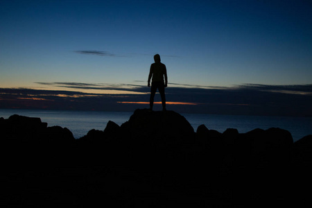 晚上，戴着帽子的人站在海背景上的岩石上。 平静宁静孤独与自然。