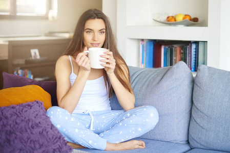 完整的镜头吸引年轻女子在家里沙发上放松和喝茶。