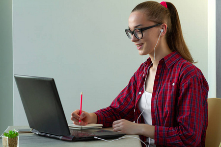 学生使用在线教育服务。 年轻的女人看着笔记本电脑，看着训练外语课程，用耳机听。 现代学习技术理念。