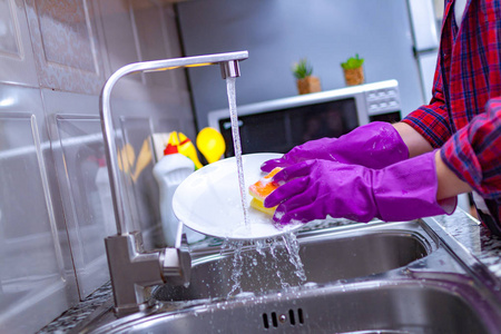 家庭主妇戴着橡胶彩色手套,在家里的厨房里用黄色海绵洗碗.照片