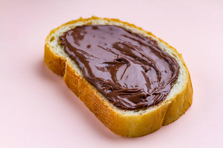 一块面包，在粉红色的背景上涂上巧克力糊。 早餐加鲜面包的甜坚果黄油。 巧克力三明治