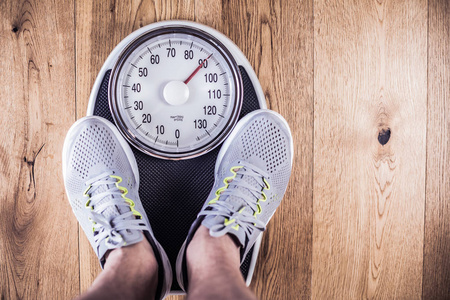 男人站在健身房的体重秤上.用卷尺测量腰部.健康生活方式的概念.照片