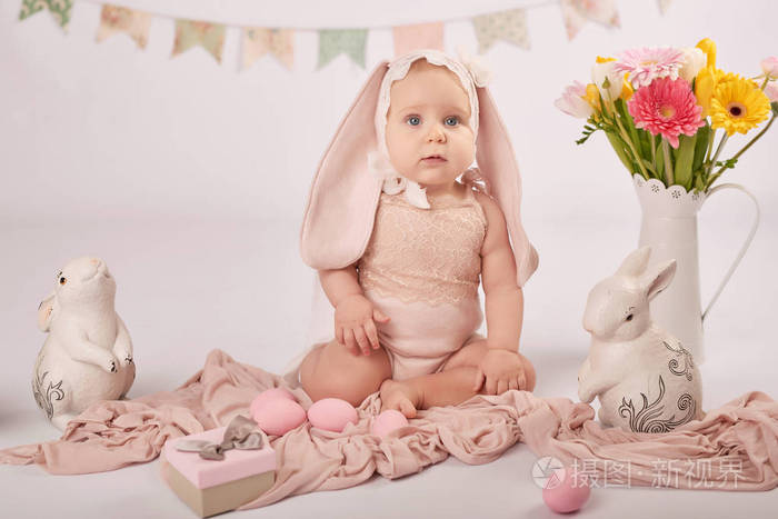 复活节婴儿穿着一套浅色背景的小可爱女孩，带兔子和鸡蛋