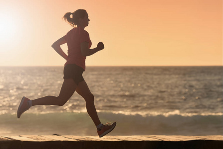早晨日出时在海滩上跑步的妇女健身运动照片