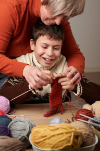 妈妈正在学习她的孩子编织。 五颜六色的羊毛纱线在木桌上。