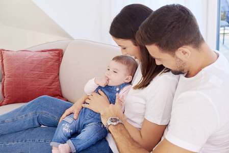 一个幸福的年轻家庭坐在沙发上和他们的女婴，享受在家放松。