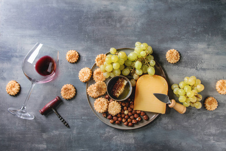 葡萄酒小吃。 奶酪，葡萄，坚果，奶酪，饼干，蜂蜜，铺设一杯红酒和刀在黑暗的纹理背景。 平躺空间