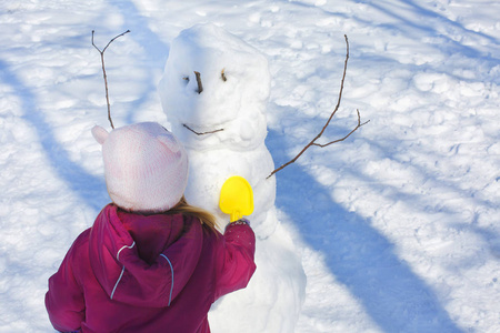 可爱的小女孩建立一个雪人在冬季公园。可爱的孩子在雪地里玩耍。孩子们的冬季活动。玩和享受雪的乐趣