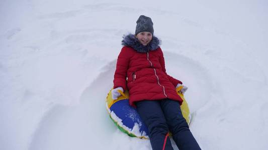 圣诞节假期, 少女在冬季公园里玩耍。女孩在冬天从高山上滑行雪橇和充气雪管。慢动作