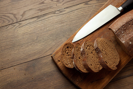创意背景，切片黑麦面包和一刀特写，放在木切板上，平躺，复制空间..新鲜糕点，黑面包的概念..