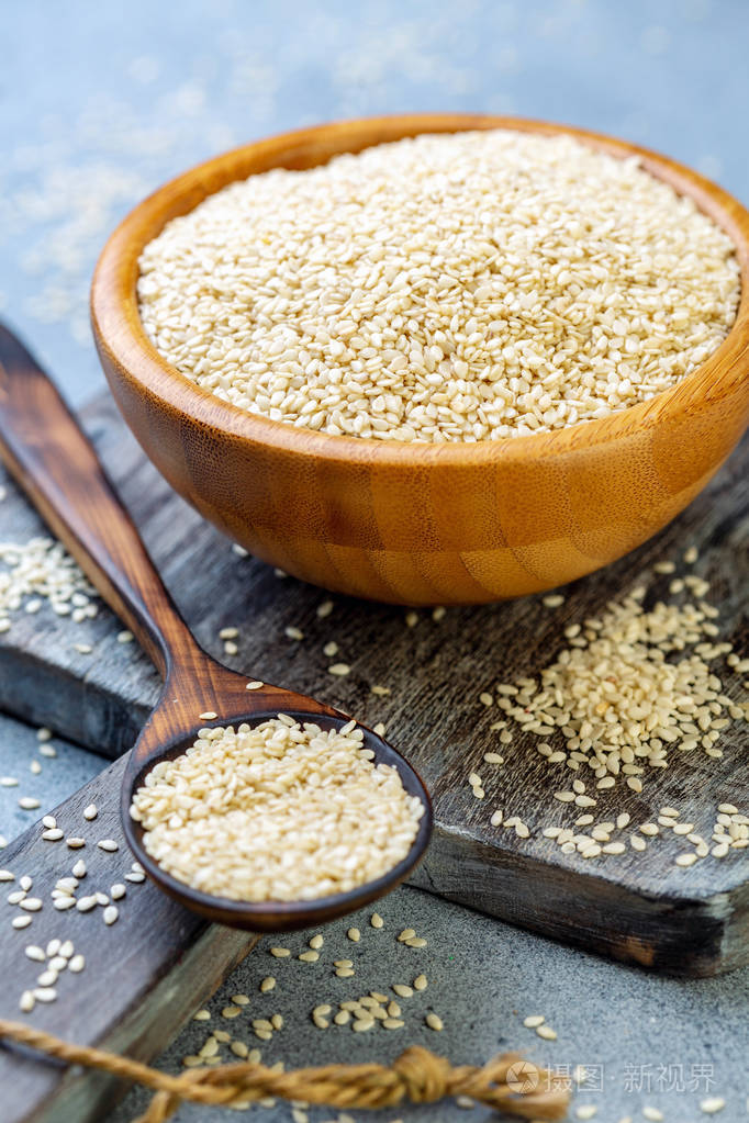 白芝麻放在木碗里,勺子放在一个旧的服务板上,选择性地聚焦.