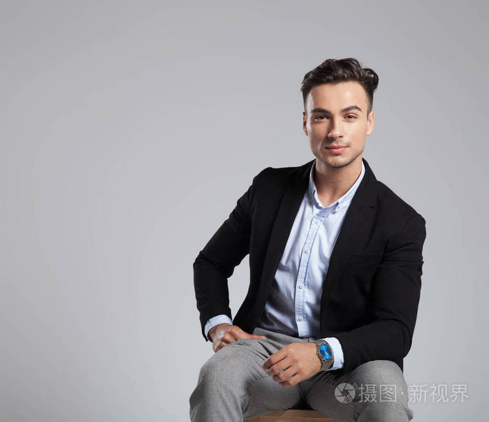 穿着黑色西装坐在浅灰色背景的木椅上的迷人商人肖像