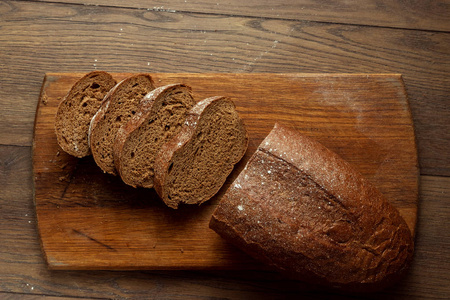 创意背景，新鲜出炉的切片黑麦面包放在木切割板上，平放，复制空间..新鲜糕点，黑面包的概念..