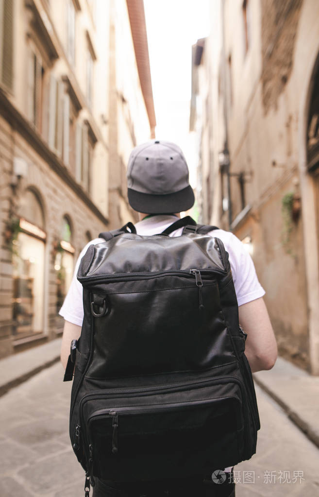一个带着一个黑色大背包的游客的肖像在城市的狭窄街道上向前看在