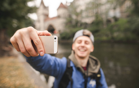 年轻的快乐游客在历史建筑和湖泊的背景下自拍，微笑。专注于智能手机