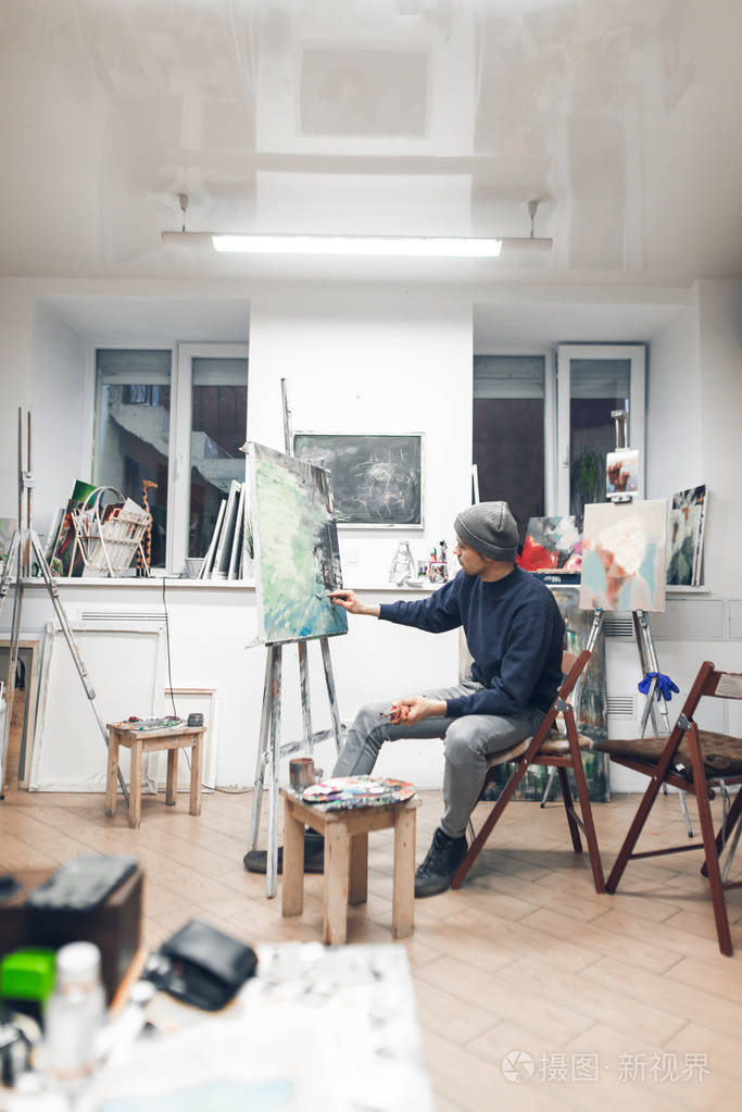 画家坐在舒适的工作室的椅子上画油画艺术家在家庭绘画工作室工作绘画