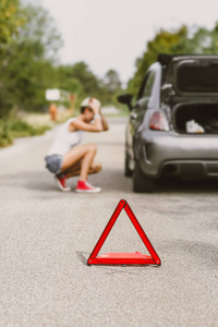 年轻漂亮的女人在路边洒了一条后轮胎。 有问题的汽车和红色三角形警告其他道路用户。