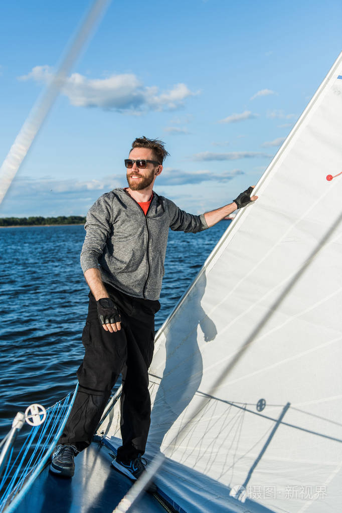 年轻的欧洲男子站在游艇边缘看海.用帆在老船上旅行.奢华生活方式