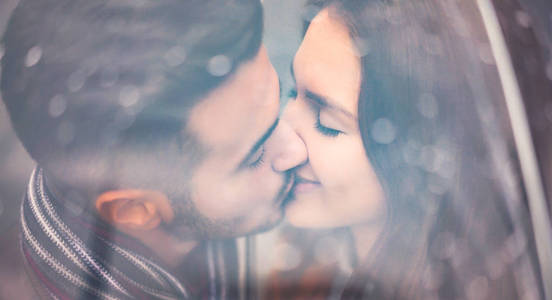 年轻夫妇在雨天的伞下接吻浪漫情人有温柔的时刻户外人们的爱情和关系观念
