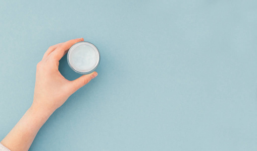 s hand holds a tube with a cream, isolated on a blue background