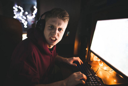 关闭肖像的情绪游戏玩家在耳机上玩电子游戏，在家庭电脑上看相机与的外观。 富有表现力的玩家玩家庭电子游戏。