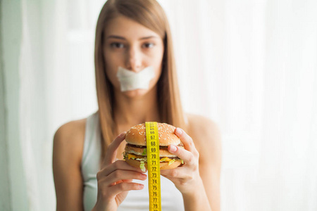 饮食。 年轻的女人嘴上有胶带，阻止她吃垃圾食品。 健康的饮食观念。