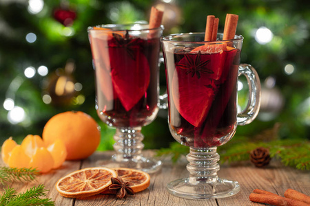 两杯圣诞覆盖葡萄酒或Gluhwein香料和橙色切片在乡村餐桌上的圣诞树。 寒假的传统饮料。