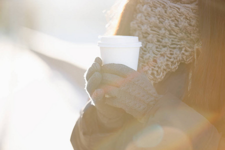 女人手里拿着温咖啡饮料。穿着暖冬衣服的女孩拿着白纸，拿走咖啡杯。把你的日志或咖啡馆的名字放在餐具上。