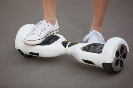 女孩脚骑电动迷你悬停板滑板车户外公园。生态城市利用电池供电，对大气无空气污染