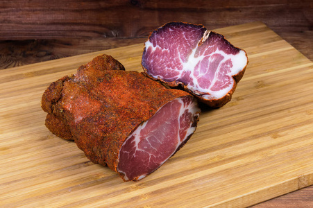 风干的肉一张深色的木制乡村餐桌上的竹制砧板上,两块干猪肉,由颈部制