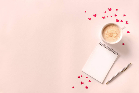杯咖啡，打开笔记本和红心粉色米色背景，复制空间。最小的平面躺着卡布奇诺咖啡和模拟书的情人节文本，爱情和浪漫的概念，顶部视图。