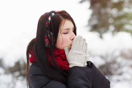 在冬天的户外，年轻女孩用温暖的呼吸温暖她冻僵的手