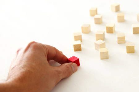 s hand moves the one different red cube block among wooden block