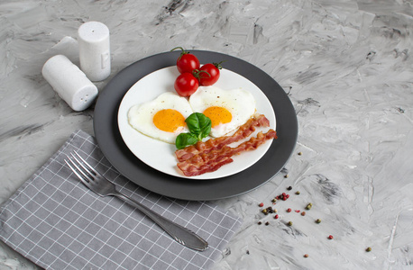 美味的煎蛋，心形的，放在一个白色盘子里，配上培根番茄罗勒椒灰底情人节早晨