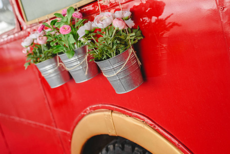 在老式汽车展览中，有装饰植物挂在红色公共汽车上的罐子。