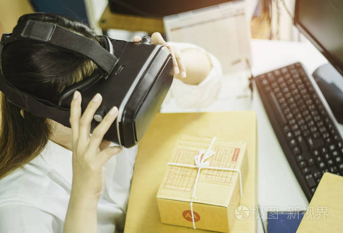 亚洲女性创业小企业主正在利用虚拟现实与纸板箱沟通，在家庭办公室在线销售理念电子商务和产品交付业务中包装产品。
