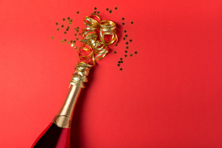 红纸背景上有金色蛇纹石的香槟瓶。 情人节生日婚礼庆祝概念。 上面的风景。 平躺着。 复制空间