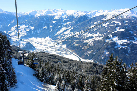 现代舒适的高山滑雪场缆车。 人们在晴天在阿尔卑斯山准备好的斜坡上滑雪。 美丽的雪山和小村庄。 家庭完美的寒假目的地。