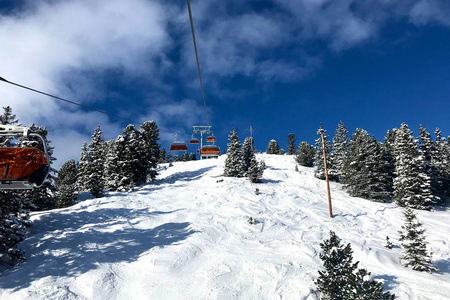 现代舒适的椅子升降机在高山滑雪胜地。 人们在晴天在阿尔卑斯山准备好的斜坡上滑雪。 在山上雪树之间的缆车。 家庭完美的寒假目的地。