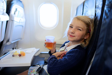 快乐的小女孩在飞机上享受美食和放松。 一家人乘飞机去度假目的地。 儿童友好航空公司。