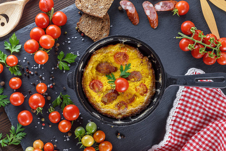 煎蛋卷用鸡肉鸡蛋和红樱桃西红柿和熏肠在圆形黑色煎锅顶部视图