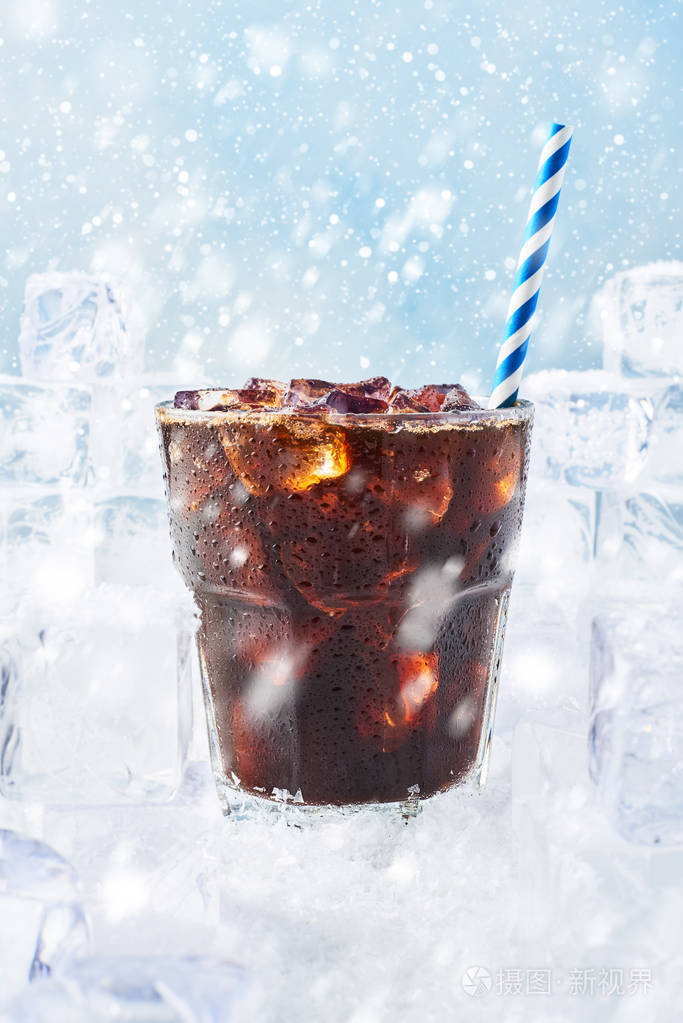 冬天喝冰咖啡在一个杯子与稻草包围在雪上的冰块蓝色
