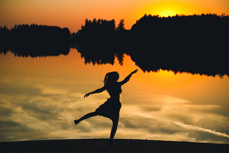一个年轻漂亮的女孩在倒影池的夕阳背景上跳跃的剪影。