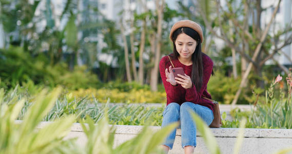 女人在城市里用手机坐在公园的长凳上。