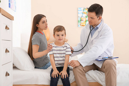 s doctor examining little patient with stethoscope at home