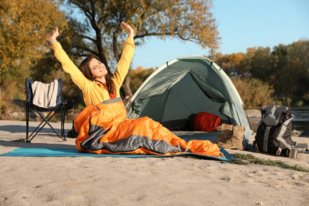 年轻女子在户外露营帐篷附近的睡袋里伸懒腰