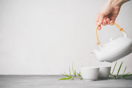 女性手把绿茶从茶壶倒入白色背景上的杯子，并有复制空间。 亚洲茶具。