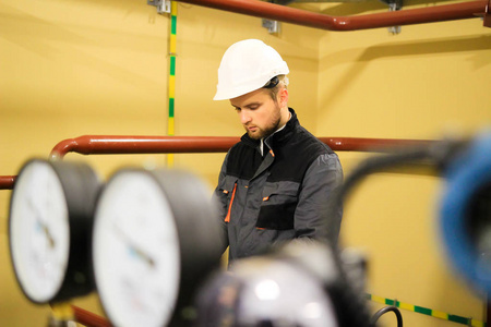 在炼油厂穿着工作服和防护头盔检查设备的工人